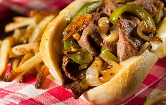 Steak sandwich with sautéed onions and green peppers served in a roll, with fries on the side