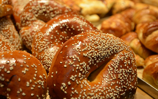 Freshly baked sesame bagels displayed on a bakery tray with a golden brown crust