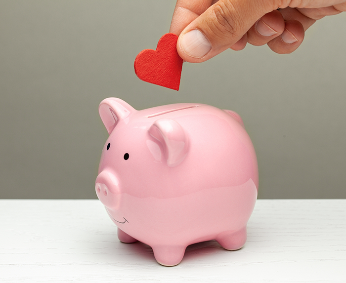 Hand placing a red paper heart in a pink piggy bank