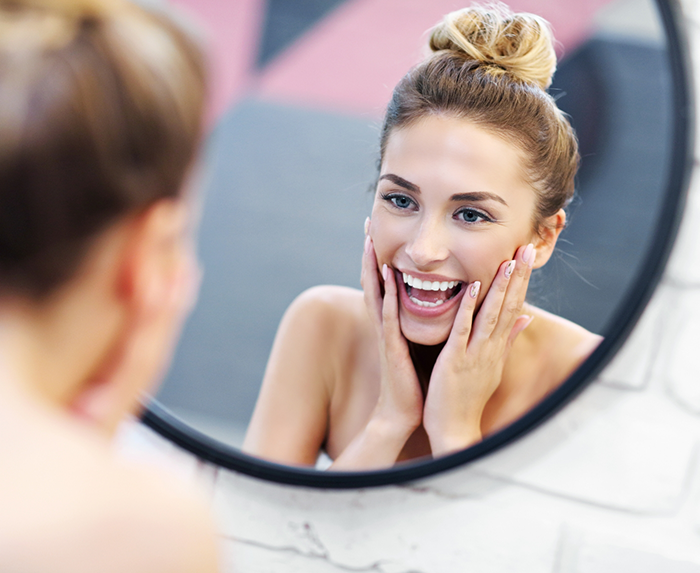 Woman looking at her smile in a mirror after cosmetic dentistry in Ocoee