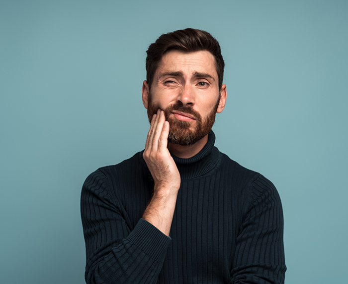 Man in a black sweater holding his cheek in pain before seeing his emergency dentist in Ocoee