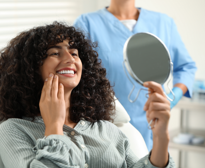 Woman looking at her smile in a mirror after receiving dental services in Ocoee