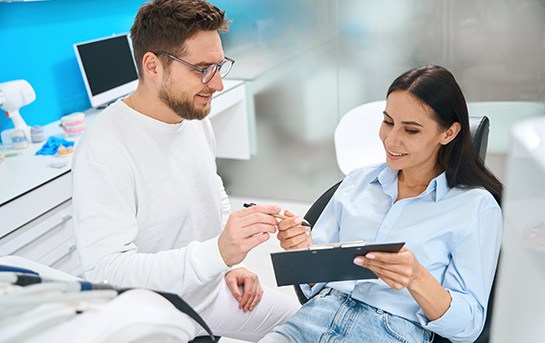 Woman in dental chair signing forms on clipboard for dentist