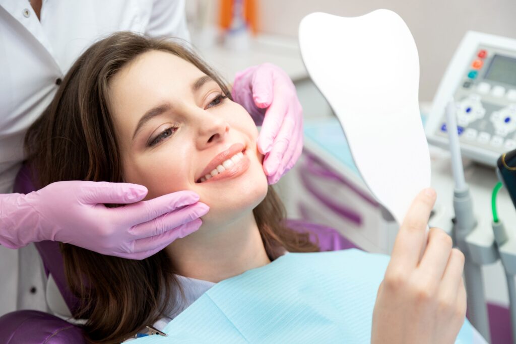 Woman in dental chair smiling into mirror with dentist touching her cheeks